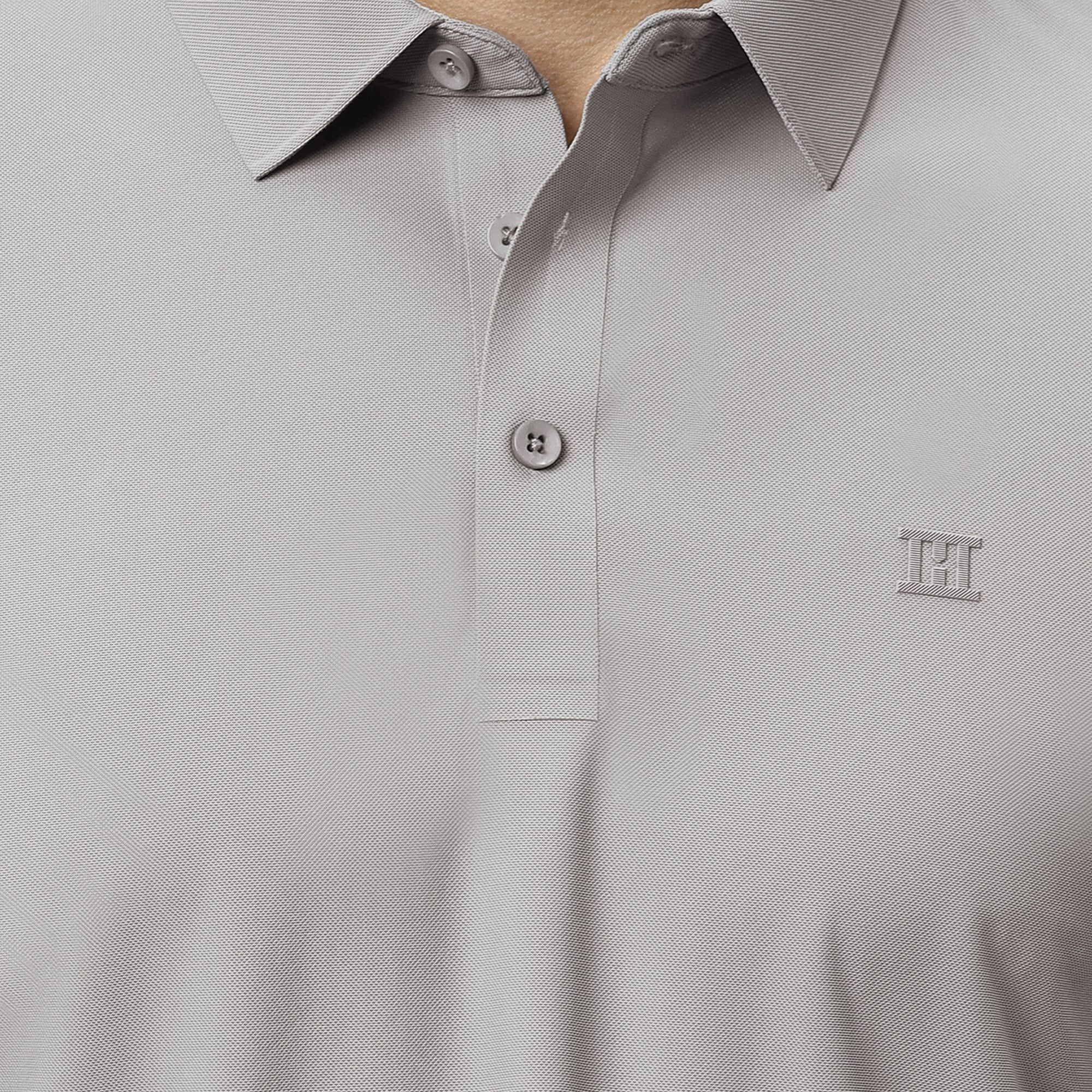 Close-up of a stone gray polo shirt with a small hektor logo on a plain background
